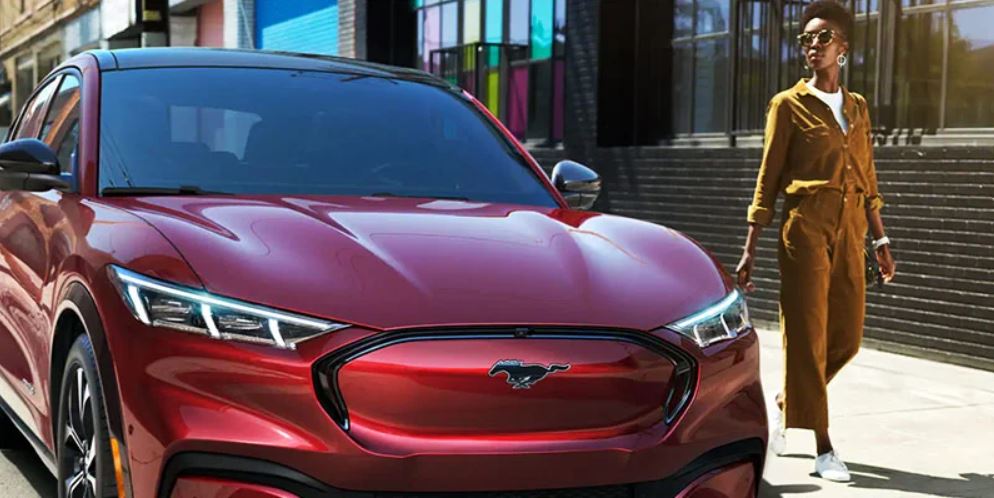 A woman walking beside a red 2021 Ford Mach-E parked on the street. | Ford service center in Little Rock, AR.