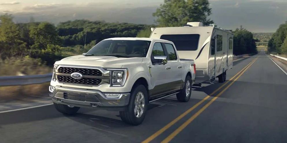 A white 2022 Ford F-150 pulling a trailer on the highway. | Ford dealer in Little Rock, AR.